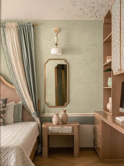 This bedroom whispers elegance with its dusty sage walls and layered textures. We designed a custom built-in desk and shelving unit next to the bed, which features a soft, arched headboard and two-toned drapery.