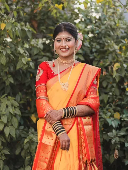 A classic portrait of the bride standing amidst lush greenery, her traditional attire looking vibrant and beautiful.