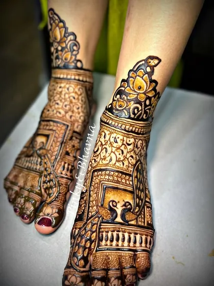 A bride's look is complete only when her feet are adorned with beautiful mehndi. Here is a close up of an intricate bridal foot design, featuring traditional jharokha windows, peacocks, and delicate jaali work, perfectly matching the hand design.