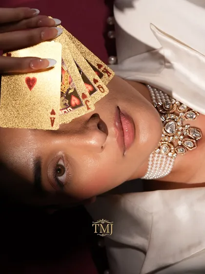 An artistic shot featuring the Polki and pearl choker with a model holding a fan of golden playing cards.