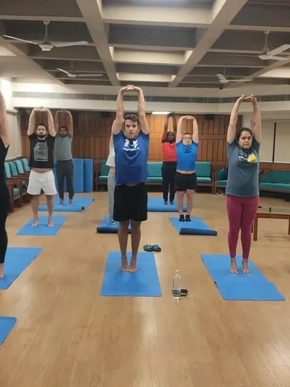 The international group practices Tadasana, a foundational standing pose. This helps in correcting posture and creating a stable base for more advanced asanas.