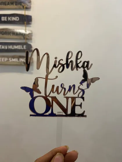 This "Mishka Turns ONE" topper in rose gold features delicate butterfly accents, perfect for a whimsical and gentle first birthday theme.