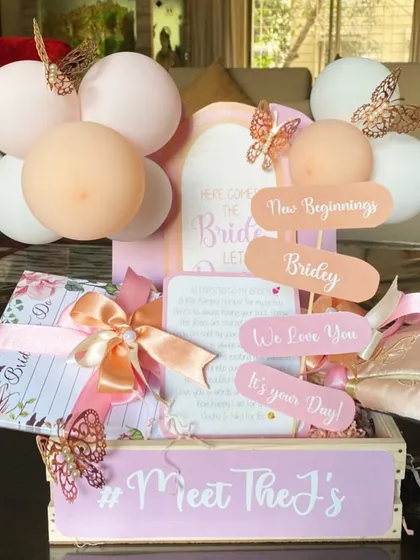 'Here comes the bride'. A beautiful crate filled with essentials for the bride-to-be, including a bridal diary and other personalized items, decorated in pastel pinks.