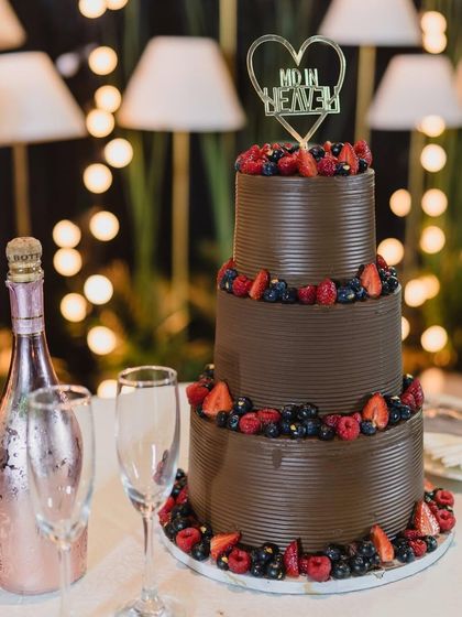 This three-tiered "Very Berry" chocolate wedding cake is ready for its moment. Adorned with fresh strawberries and blueberries and a "Made in Heaven" topper, it’s perfect for a sophisticated evening reception.