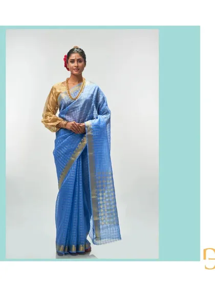 This ethereal cornflower blue silk organza saree is paired with a traditional gold blouse, highlighting its versatility. The gold zari checks add a touch of luxury.