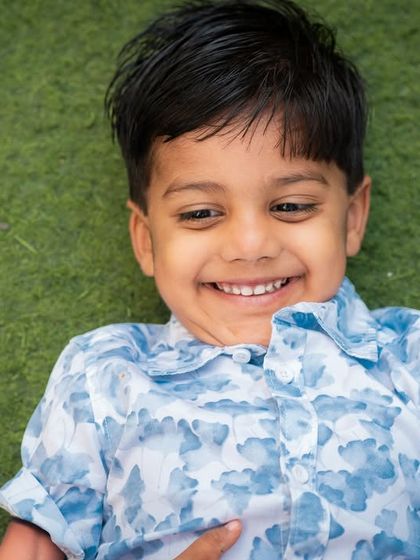 A close-up shot of a boy's infectious smile. Lying on the grass, this candid moment is full of pure, simple joy.