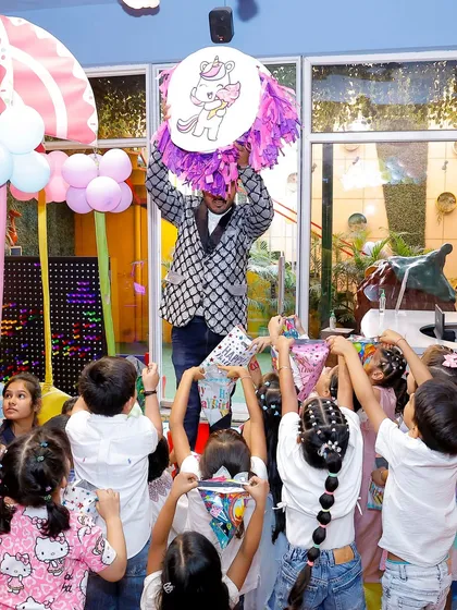 The unicorn-themed piñata bursts open, showering the excited children with treats. It's a moment of high energy and fun for everyone.