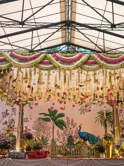 A full view of the traditional South Indian mandap, showcasing the intricate floral torans, classic temple pillars, and the beautiful hand-painted backdrop. We draped the ceiling in soft green fabric to complement the natural surroundings.