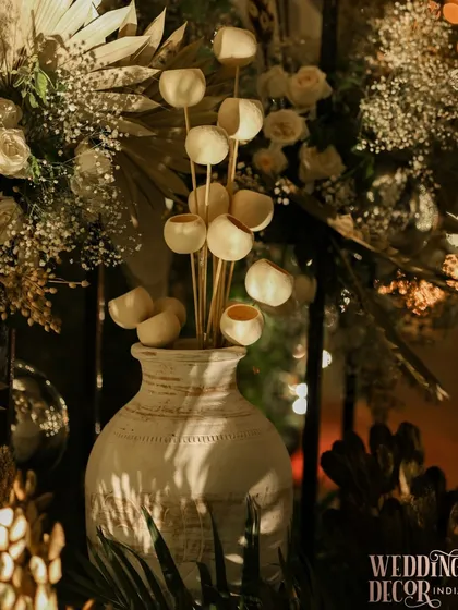 A close-up of a decor detail, featuring dried lunaria flowers in a rustic white vase. The interplay of light and shadow highlights the textures and natural beauty of the elements.