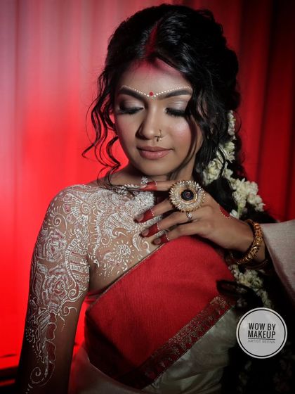 A close-up of the traditional Bengali makeup, featuring the large red bindi and intricate white alta designs on the arm.