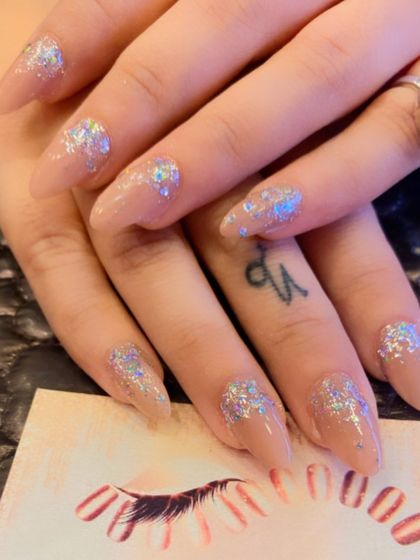 A chic and sparkly design on long stiletto nails. The sheer nude base is enhanced with chunky silver holographic glitter flakes for a bold, modern look.