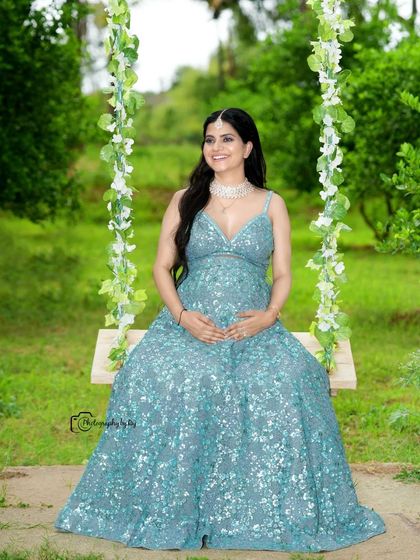 A glamorous shot of a mother-to-be in a sparkling blue gown, seated on our floral swing.