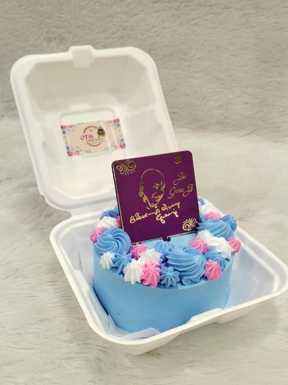 A colorful bento cake for Guruji's birthday, with swirls of blue, pink, and white frosting, topped with a special edible plaque.
