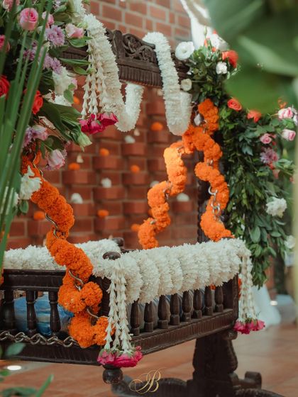 A closer look at the cradle decor, highlighting the layers of white jasmine and orange marigold garlands against the dark wood of the traditional cradle.