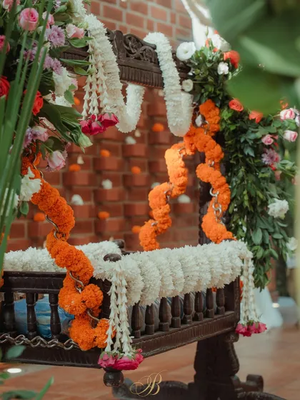 A closer look at the cradle decor, highlighting the layers of white jasmine and orange marigold garlands against the dark wood of the traditional cradle.