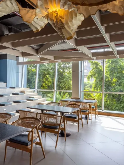 The Paras Healthcare office in Gurugram is anchored in simplicity, light, and nature. This breakout area features tiered seating overlooking a full-height window with lush green views, blurring the boundary between the built environment and the outdoors.