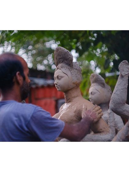 A sculptor carefully shapes the clay of a Durga idol. This behind-the-scenes shot documents the immense skill and devotion that goes into creating these sacred figures.