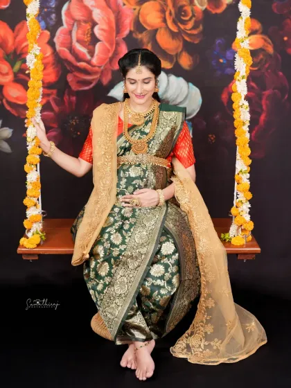 A graceful portrait of a mother-to-be on a swing, draped in a traditional green saree. The floral backdrop adds a touch of softness and romance to this elegant shot.