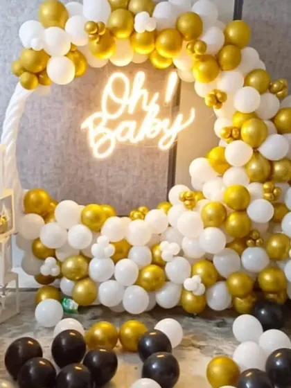 A chic baby shower decoration with a "Oh! Baby" neon sign. The circular frame is filled with white, gold, and black balloons, and complemented by transparent "BABY" blocks.