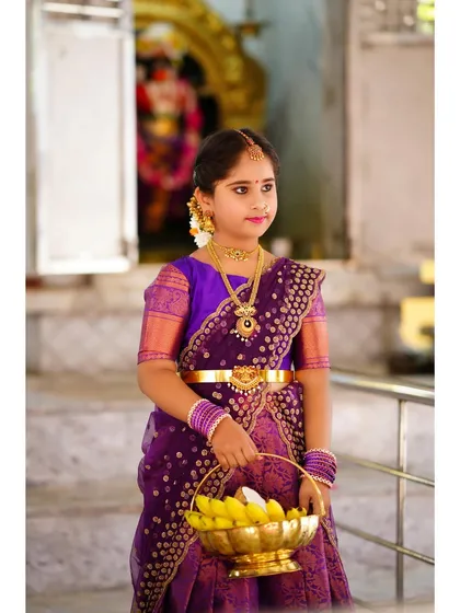 A young girl dressed in a beautiful traditional purple saree for a temple visit, holding a basket of bananas. A perfect way to capture cultural milestones.