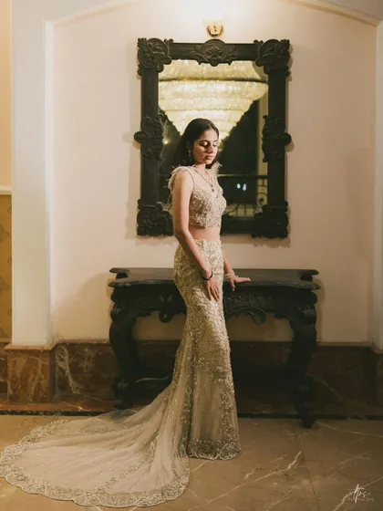 A full-length portrait of Anmol, showcasing the intricate details of her gown against a classic interior. The lighting is focused to create a soft yet striking image.