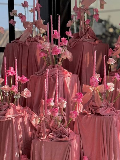 An artful installation of pink candles, ribbons, and flowers set on pedestals draped in luxurious pink velvet. This multi-level display creates visual interest and reinforces the event's sophisticated, monochromatic theme.