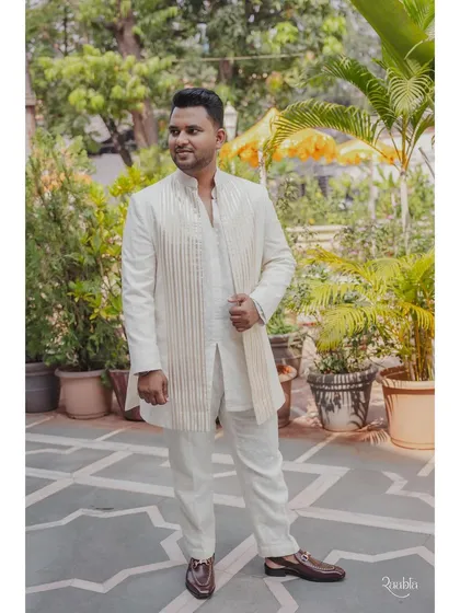The groom's full look for the pooja. The custom-made white kurta is paired with a matching striped jacket, creating a layered and sophisticated traditional outfit.