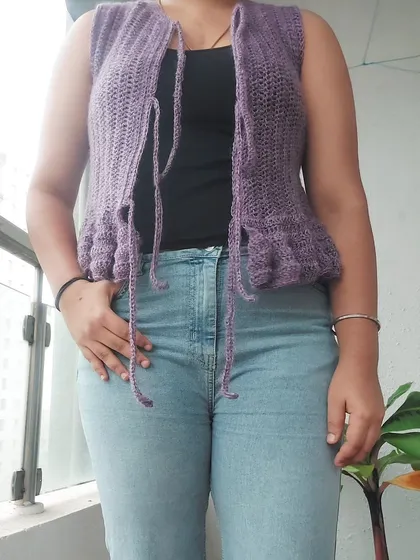 This is the Azula Top, a delicate vest made with soft mohair yarn. It features a peplum ruffle and multiple tie-front closures.