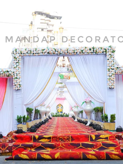 A classic and elegant wedding entrance. The walkway is framed by a beautiful arch of white flowers, with flowing white drapes and chandeliers creating a grand passage for guests.