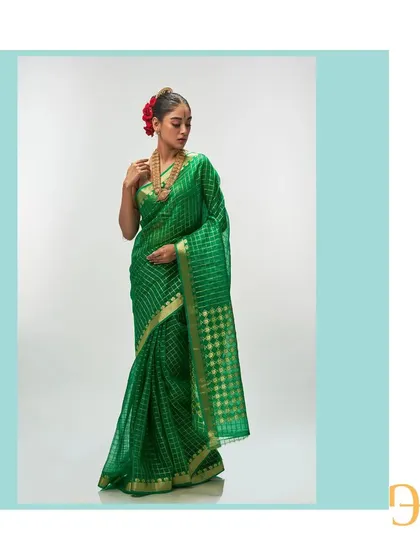 The vibrant shamrock green of this silk organza saree from the Champa collection is truly captivating. Delicate gold zari checks adorn the fabric, offering a festive and luxurious feel that is both lightweight and visually striking.