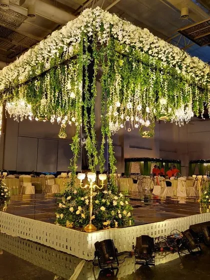 For a more contemporary feel, I created this elegant wedding mandap featuring a cascade of white flowers and fresh greenery. The mirrored pillars and soft lighting give it a sophisticated and modern look, perfect for an indoor convention hall setting.