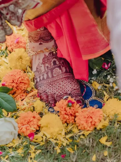 The bride's foot, decorated with a dark henna stain, amidst a bed of flowers during a wedding ceremony.