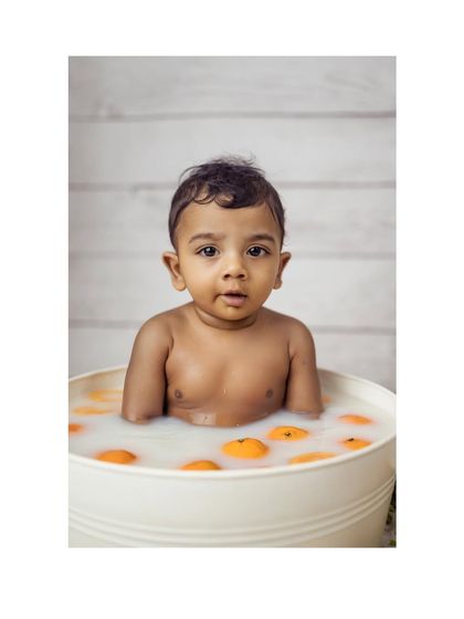 A sweet portrait of a baby boy looking up from his orange-filled milk bath. The simple white background keeps the focus on his innocent expression.