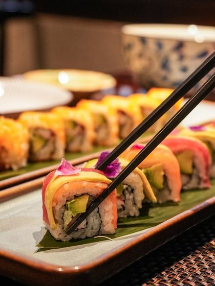 A guest enjoying a piece of our Rainbow Sushi Roll. Each bite offers a harmonious blend of fresh fish, creamy avocado, and perfectly seasoned rice, making it one of our most popular dishes.