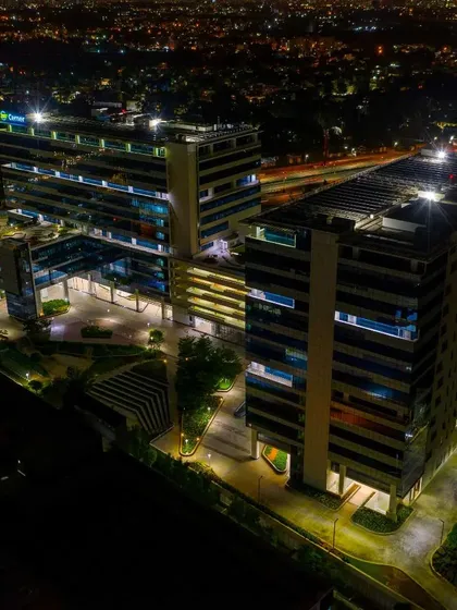 A high-angle aerial shot of a modern office complex at night, revealing the intricate design of the building and its landscaped surroundings against the city glow.
