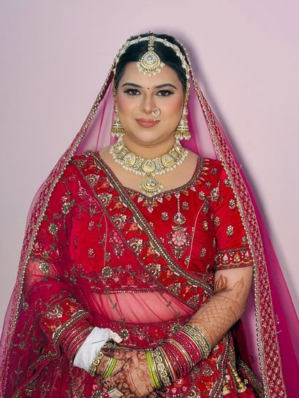 A portrait of the bride against a simple background, making her red lehenga and radiant makeup the center of attention.