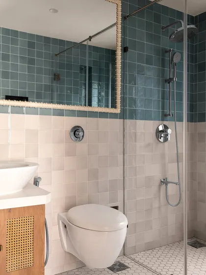 This bathroom features a mix of handmade-look tiles in blue and white, creating a serene and slightly rustic feel. The floating wood and cane vanity adds warmth and texture to the space.