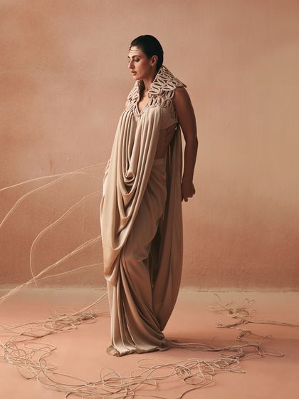 The Kashar tunic, with its statement corded collar, anchors a fluid cowl-drape against pleated satin, creating an avant-garde balance of weight and whisper.