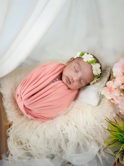 Wrapped in a soft pink swaddle, this baby sleeps under a delicate white canopy. The pink blossoms in the foreground add a lovely, soft touch to the composition.