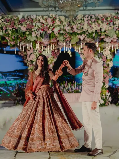 A dance between the couple at their reception. The bride's paisley-printed lehenga in muted tones and the groom's sleek blush bandhgala jacket create an elegant and romantic look, perfect for an evening celebration.