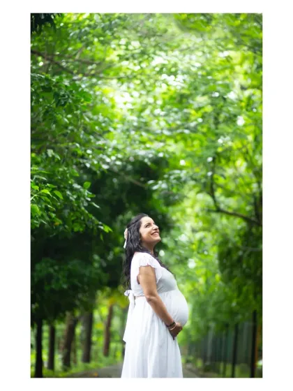 A stunning solo portrait of the mother-to-be looking up towards the sky, framed by a canopy of green leaves, capturing a moment of peaceful anticipation.