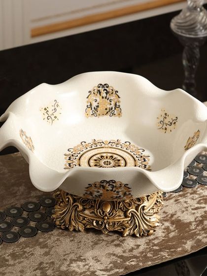 A beautiful serving bowl with a fluted edge and intricate gold patterns on a cream base. The ornate pedestal adds height and grandeur, making it a stunning piece for serving guests.