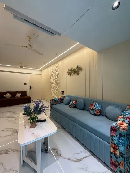 A wide view of the living room, featuring a comfortable blue sofa with floral accents, a sleek center table, and a textured feature wall. The layout is designed to be both social and relaxing.