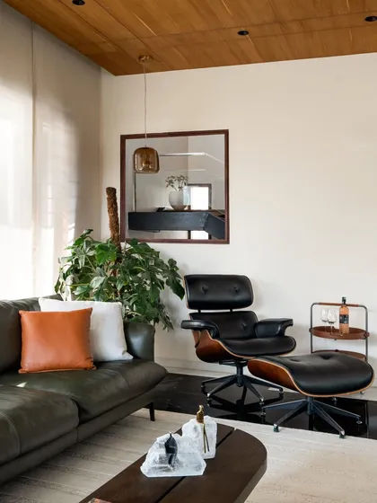 A cozy corner in one of the living spaces, featuring an iconic lounge chair and ottoman. The material palette is warm and inviting, with leather, wood, and indoor plants creating a comfortable and stylish nook.