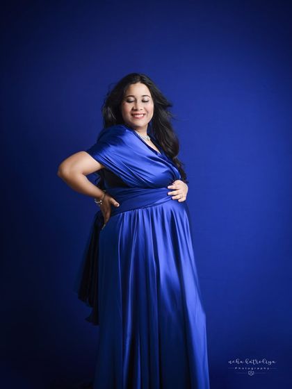 A quiet moment of joy. This portrait focuses on the mother-to-be's happy expression, with the rich blue gown providing a beautiful, vibrant frame.