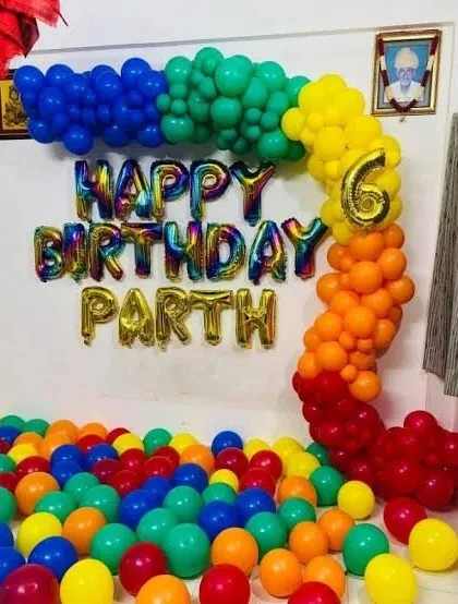 A simple yet vibrant rainbow-themed birthday decoration at home. A colorful balloon arch is paired with 'Happy Birthday' foil letters and a floor covered in balloons for a fun, playful feel.