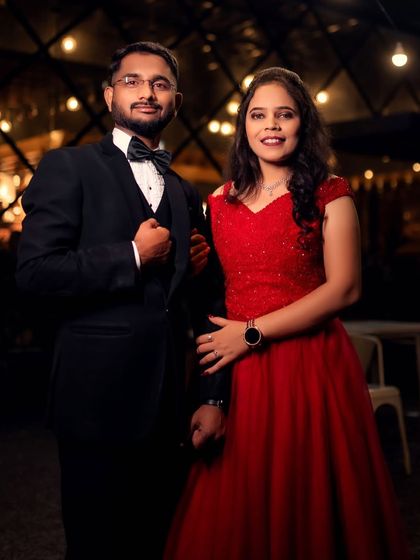 A classic couple portrait with a warm, romantic glow. The red ball gown and black tuxedo are a timeless choice for any engagement or pre-wedding event.