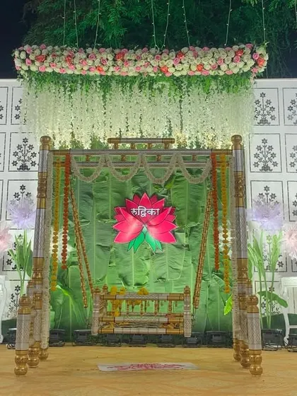 This is a complete stage setup for a traditional naming ceremony. The design centers around the beautifully decorated palna, framed by a fresh green backdrop, hanging florals, and soft lighting to create a peaceful and celebratory atmosphere.