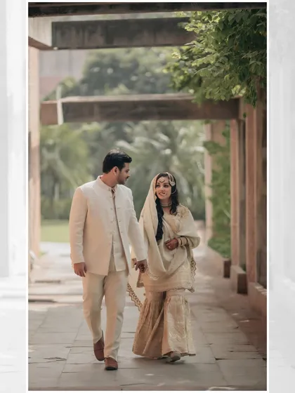 The couple walks hand-in-hand through a sunlit corridor, their smiles and gentle hold capturing a moment of pure, serene love.