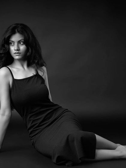 A beautiful black and white portrait of a model seated on the floor. The composition is elegant and the lighting is soft and moody.